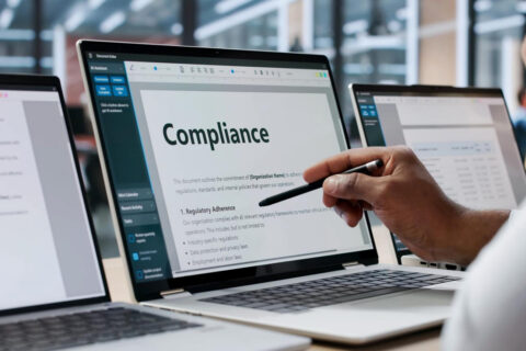 A person points at a computer screen that displays the word "compliance"